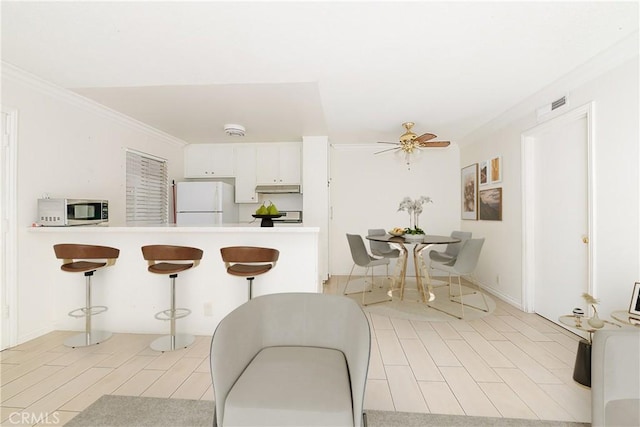 kitchen featuring kitchen peninsula, ceiling fan, ornamental molding, white refrigerator, and white cabinets