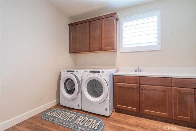 clothes washing area featuring cabinets, sink, washing machine and clothes dryer, and light wood-type flooring