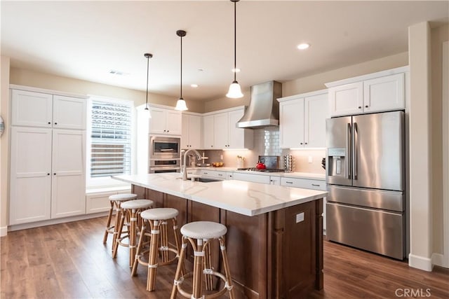 kitchen featuring appliances with stainless steel finishes, sink, white cabinets, a kitchen island with sink, and wall chimney range hood