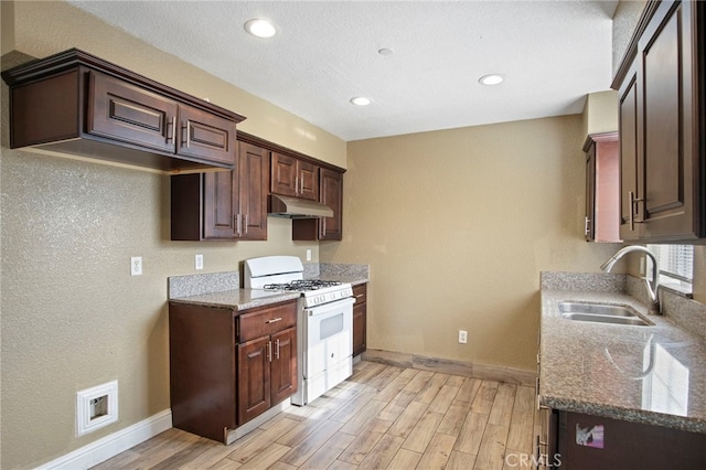 kitchen featuring stone counters, white range with gas stovetop, sink, light hardwood / wood-style floors, and dark brown cabinetry