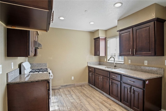 kitchen with gas stove, sink, light hardwood / wood-style floors, extractor fan, and dark brown cabinets