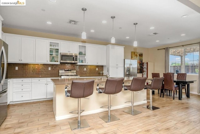 kitchen featuring a center island with sink, light hardwood / wood-style floors, decorative light fixtures, and appliances with stainless steel finishes