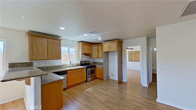 kitchen with appliances with stainless steel finishes, sink, kitchen peninsula, light hardwood / wood-style floors, and dark stone countertops