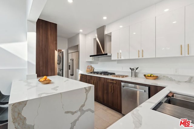 kitchen featuring light stone counters, dark brown cabinets, wall chimney range hood, and stainless steel appliances