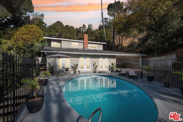 pool at dusk with french doors and a patio