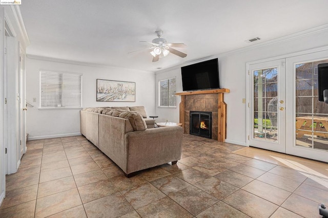 living room featuring a tiled fireplace, ceiling fan, a healthy amount of sunlight, and ornamental molding