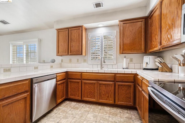 kitchen with appliances with stainless steel finishes, a wealth of natural light, tile counters, and sink