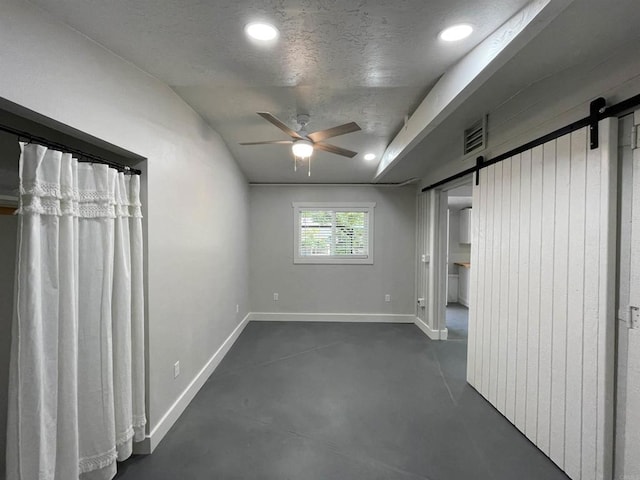 interior space with ceiling fan, a textured ceiling, and a barn door