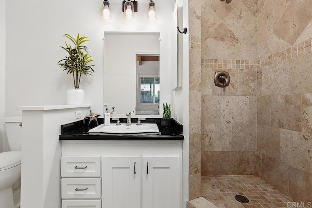 bathroom with toilet, vanity, and tiled shower