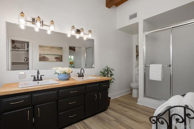 bathroom with toilet, vanity, wood-type flooring, beamed ceiling, and a shower with shower door