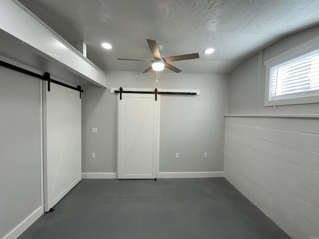 unfurnished bedroom featuring a textured ceiling, ceiling fan, and a barn door