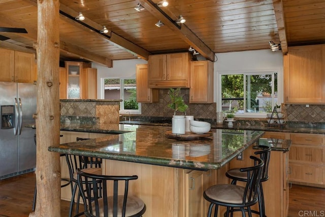 kitchen featuring stainless steel fridge with ice dispenser, dark hardwood / wood-style floors, track lighting, dark stone counters, and a kitchen island