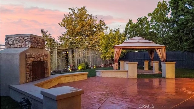 patio terrace at dusk featuring a gazebo and an outdoor stone fireplace