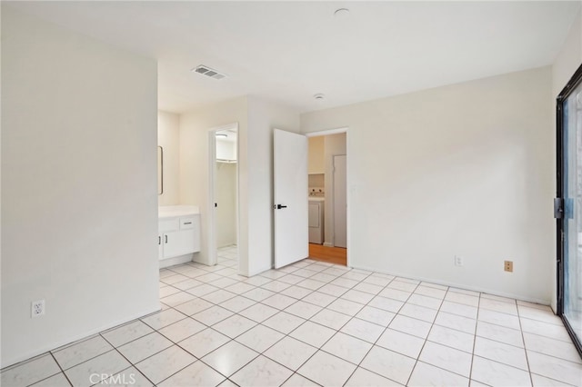 unfurnished bedroom featuring washer / dryer, ensuite bath, and light tile patterned flooring