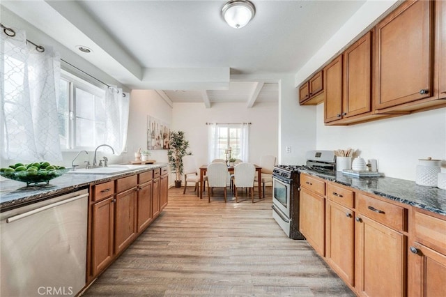 kitchen with beam ceiling, dark stone countertops, sink, appliances with stainless steel finishes, and light hardwood / wood-style floors