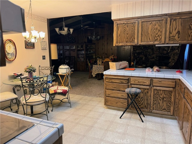 kitchen featuring tile counters, decorative light fixtures, ceiling fan with notable chandelier, and vaulted ceiling