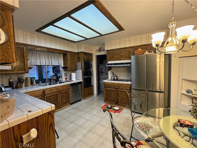 kitchen featuring tile countertops, stainless steel appliances, backsplash, decorative light fixtures, and a skylight