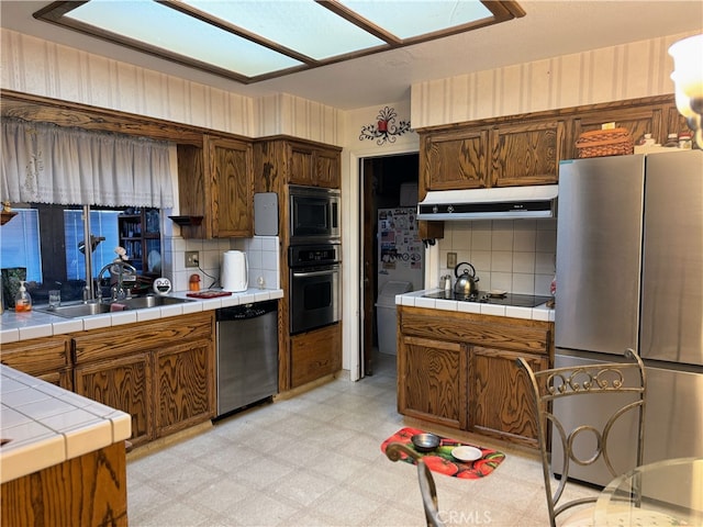 kitchen with tile countertops, stainless steel appliances, decorative backsplash, and sink