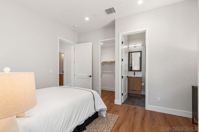 bedroom with a spacious closet, a closet, ensuite bathroom, and dark wood-type flooring