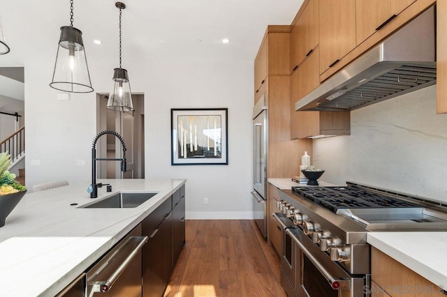 kitchen with sink, hardwood / wood-style flooring, hanging light fixtures, light stone countertops, and premium appliances