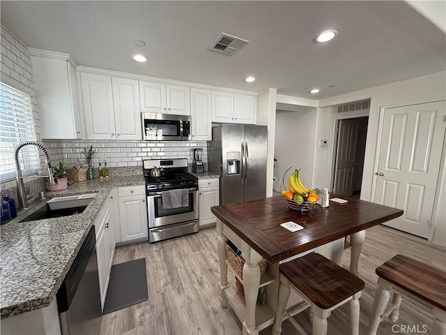 kitchen with light wood-type flooring, light stone counters, stainless steel appliances, sink, and white cabinetry