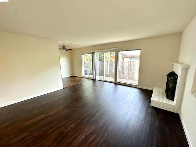 unfurnished living room featuring ceiling fan, a brick fireplace, and dark hardwood / wood-style floors