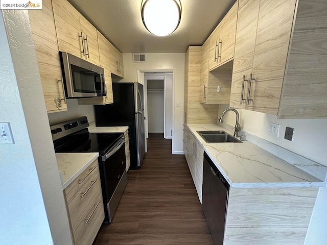 kitchen with appliances with stainless steel finishes, light stone countertops, light brown cabinetry, dark hardwood / wood-style floors, and sink