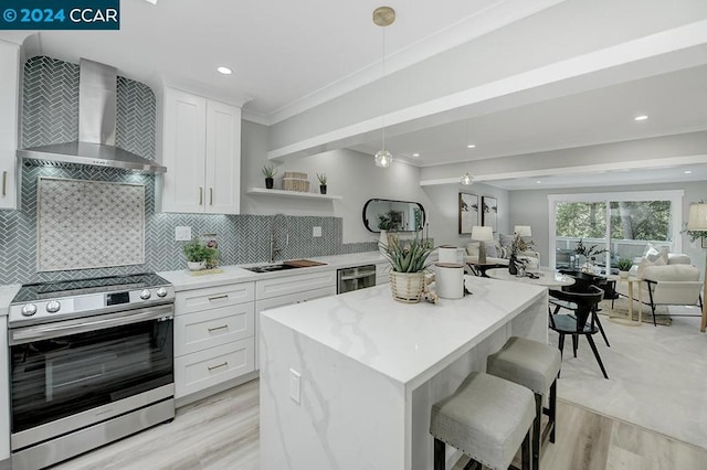 kitchen featuring tasteful backsplash, light wood-type flooring, wall chimney exhaust hood, stainless steel range, and crown molding