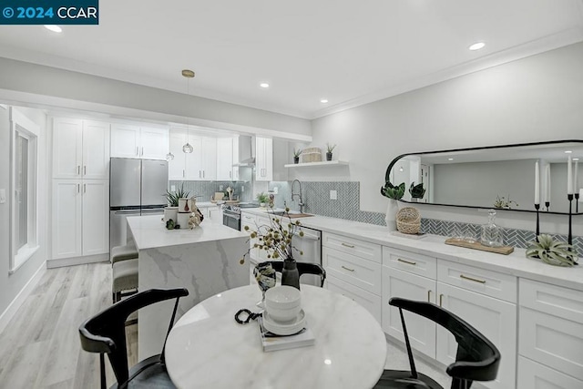 kitchen with stainless steel appliances, sink, pendant lighting, white cabinetry, and light hardwood / wood-style floors