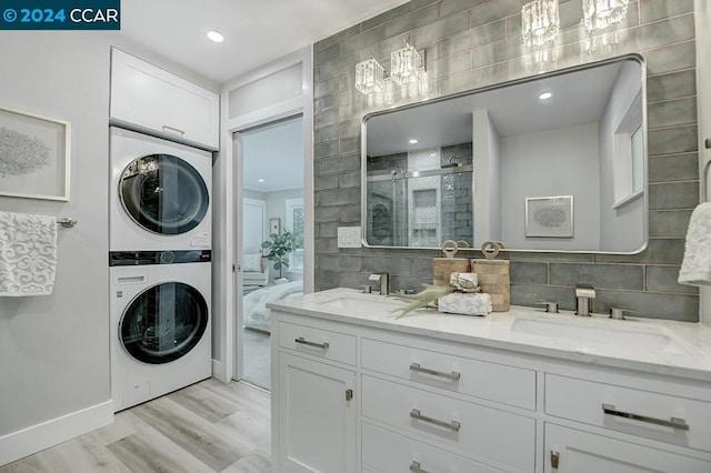 clothes washing area with sink, stacked washer / drying machine, and light wood-type flooring