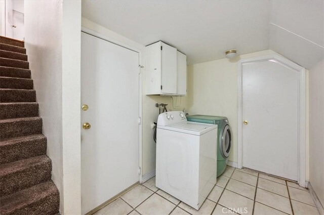 clothes washing area with washer and clothes dryer, cabinets, and light tile patterned floors