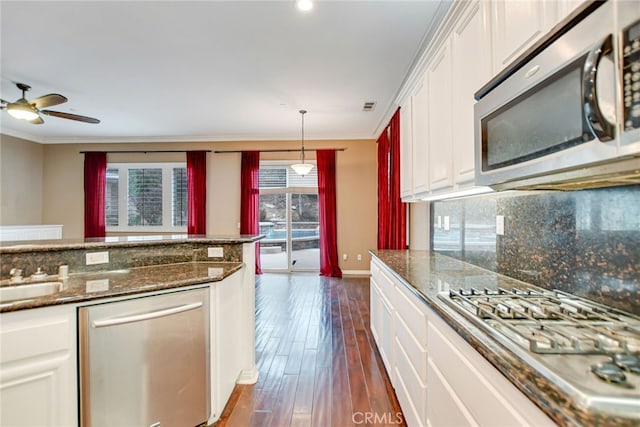 kitchen with appliances with stainless steel finishes, white cabinetry, decorative light fixtures, crown molding, and dark hardwood / wood-style floors