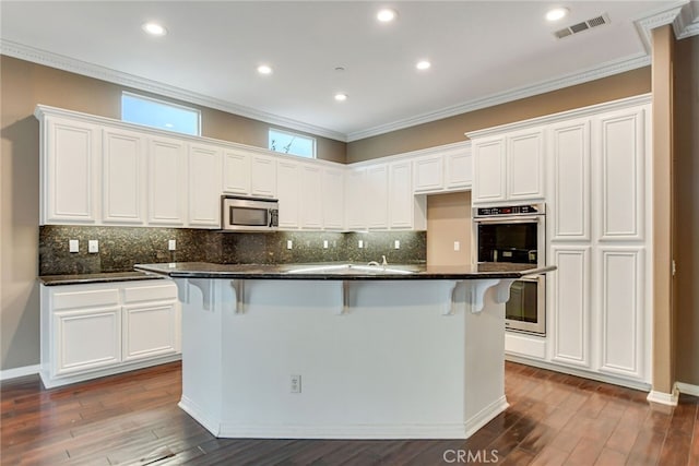 kitchen with white cabinetry, stainless steel appliances, ornamental molding, and a kitchen island