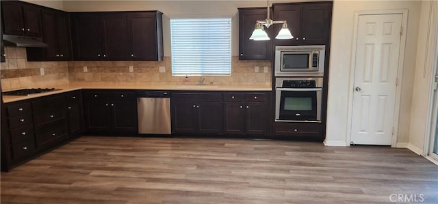 kitchen with sink, appliances with stainless steel finishes, hanging light fixtures, light hardwood / wood-style floors, and decorative backsplash