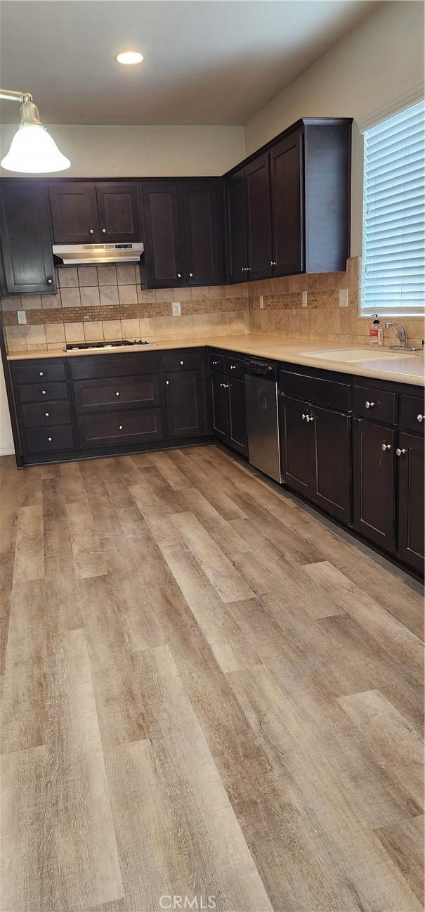 kitchen featuring sink, gas stovetop, light hardwood / wood-style floors, decorative backsplash, and stainless steel dishwasher