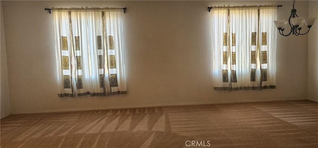 carpeted empty room with an inviting chandelier and plenty of natural light