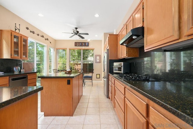 kitchen featuring stainless steel appliances, dark stone counters, ventilation hood, a center island, and tasteful backsplash