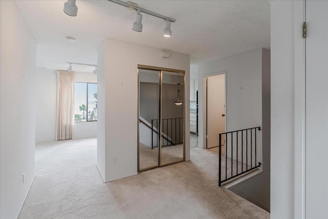 hall featuring a textured ceiling, light colored carpet, and track lighting