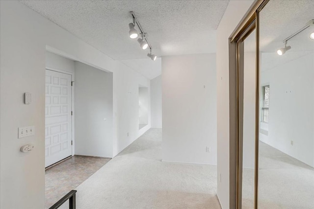 hall with a textured ceiling, rail lighting, and light carpet