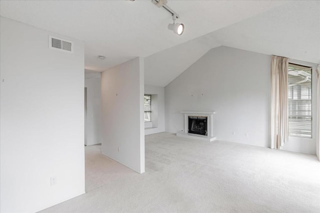 unfurnished living room with light colored carpet, track lighting, and lofted ceiling