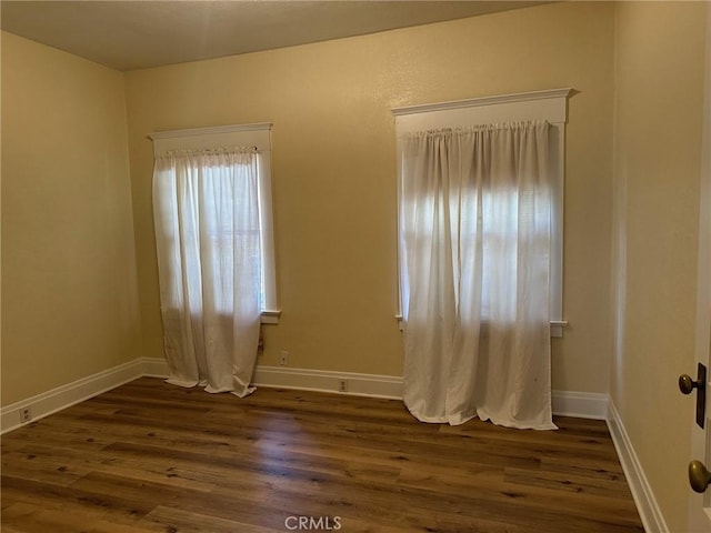 unfurnished room with baseboards and dark wood finished floors