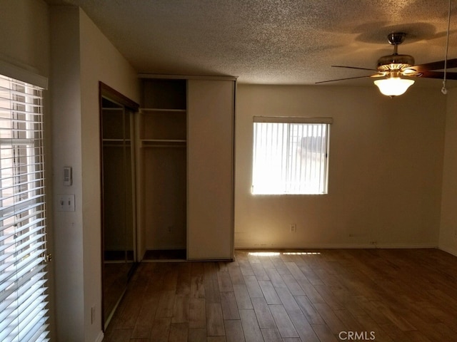 unfurnished bedroom with dark wood-type flooring, a textured ceiling, a closet, and ceiling fan