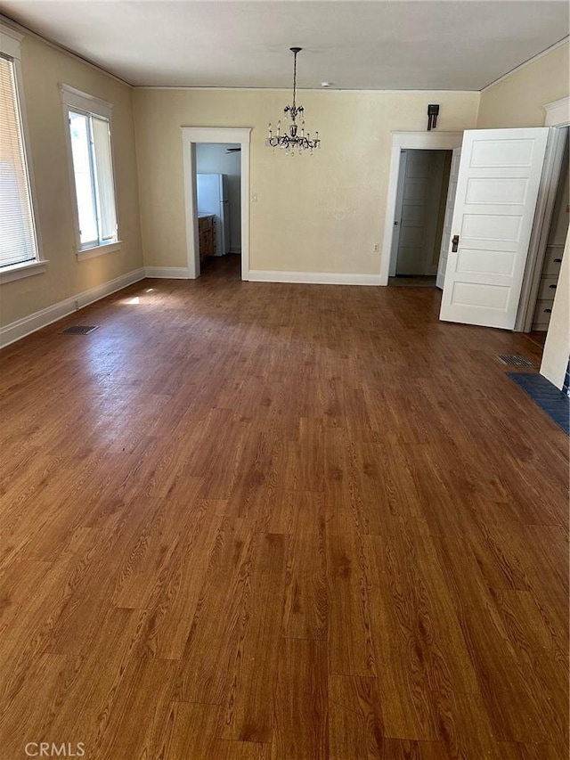 spare room with dark wood finished floors, a chandelier, baseboards, and visible vents