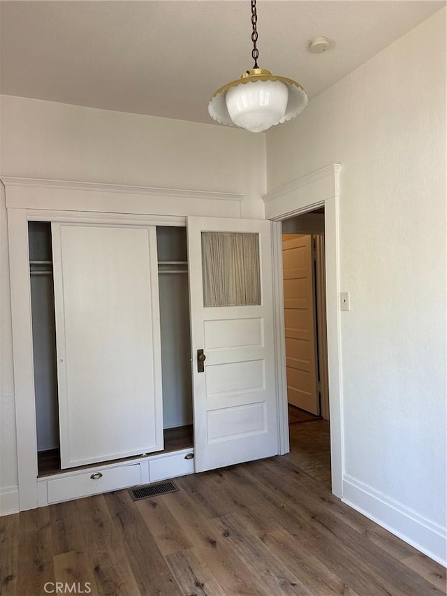 unfurnished bedroom featuring a closet, baseboards, visible vents, and wood finished floors