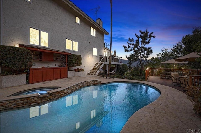 pool at dusk with exterior bar, an in ground hot tub, and a patio