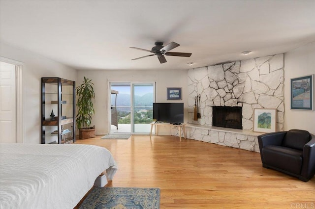 bedroom featuring access to exterior, light hardwood / wood-style flooring, ceiling fan, and a fireplace