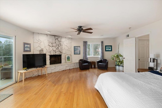 bedroom with hardwood / wood-style flooring, ceiling fan, a stone fireplace, and multiple windows