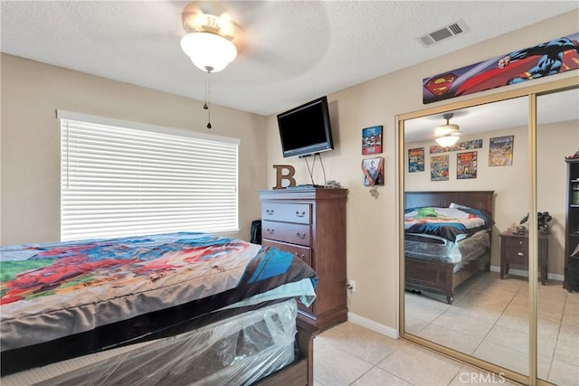 bedroom featuring light tile patterned flooring, a closet, ceiling fan, and a textured ceiling