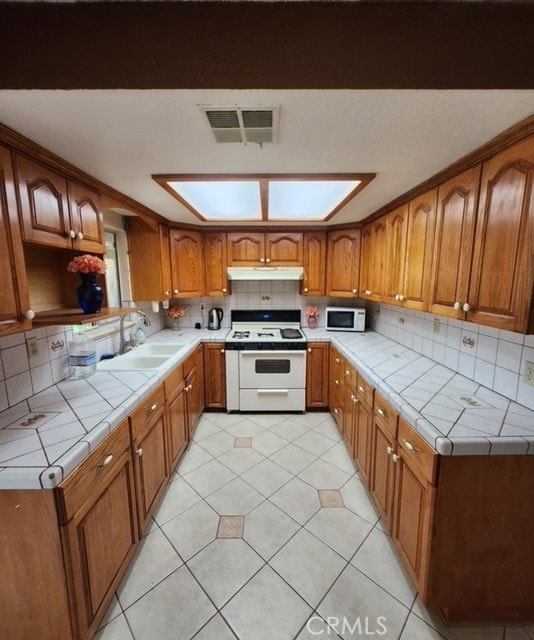 kitchen featuring white appliances, sink, a skylight, backsplash, and tile counters