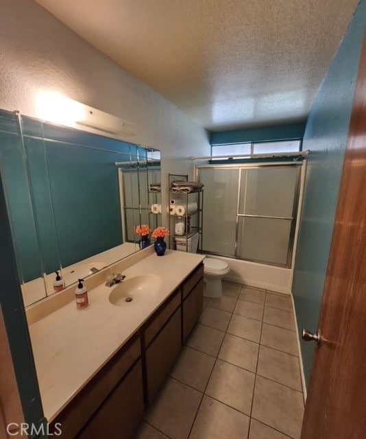 full bathroom with a textured ceiling, shower / bath combination with glass door, toilet, vanity, and tile patterned flooring